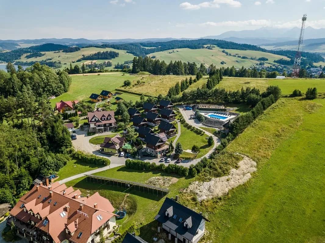 Ujęcie z drona na cały resort z domkami i basenem na tle gór