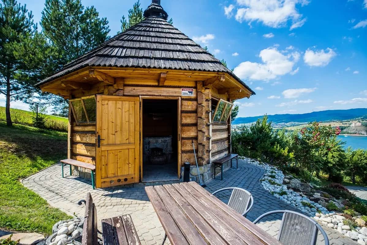 Drewniana altana grillowa z otwartymi drzwiami nad jeziorem