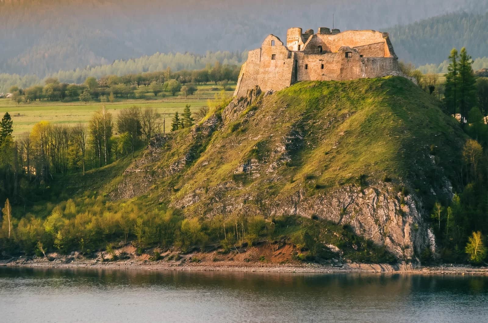 Ruiny średniowiecznego zamku Czorsztyn na skalistym wzgórzu - wapienne mury z cylindryczną wieżą nad taflą zielonego jeziora, w tle Tatry
