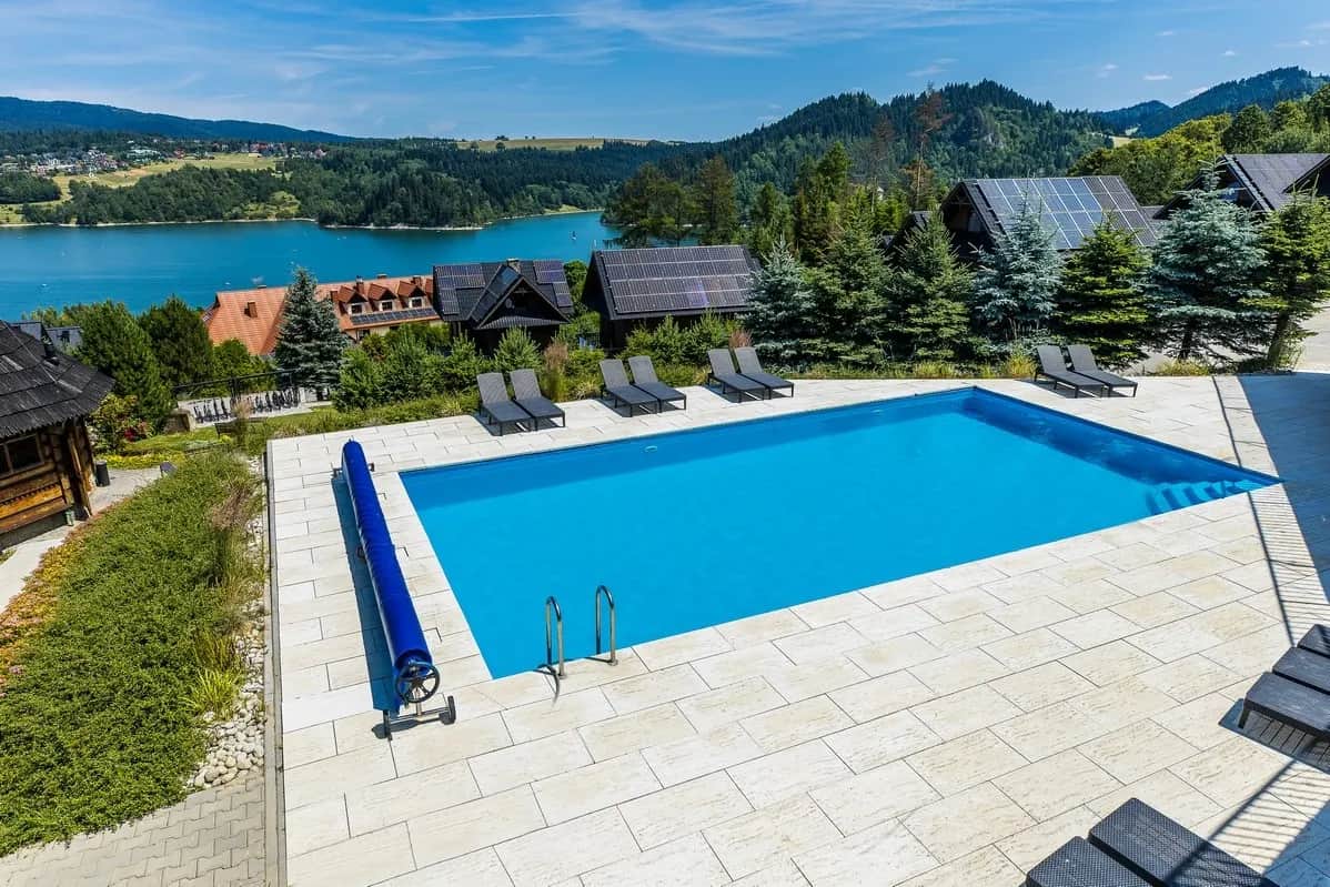Pool mit Windschutz und Liegen, im Hintergrund See und bewaldete Hügel