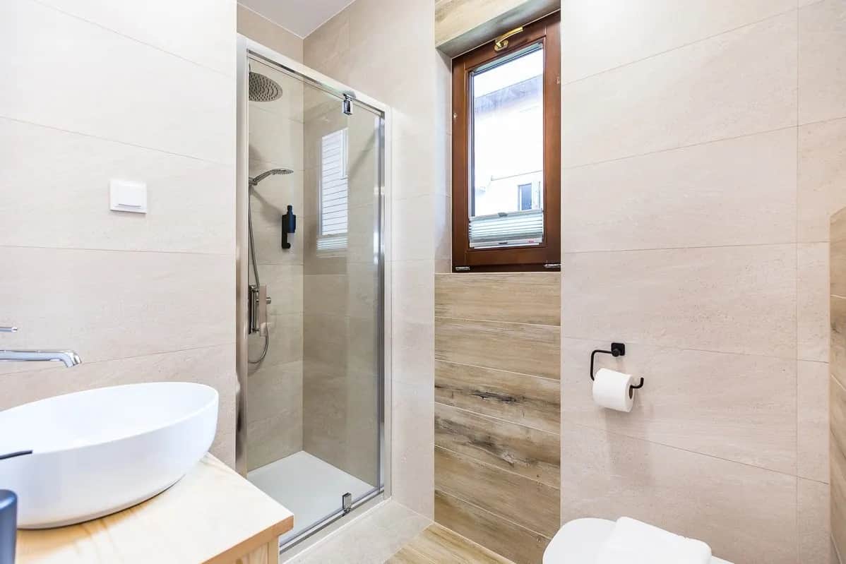 Helles Bad mit Dusche und Fenster, verkleidet mit Fliesen und Holz