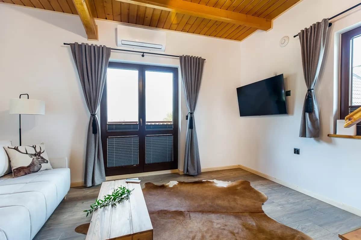 Geräumiges Wohnzimmer mit weißem Sofa, Fernseher und Holzdecke