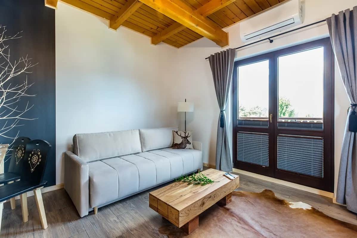 Wohnzimmer mit hellem Sofa und Balkonzugang hinter Jalousien