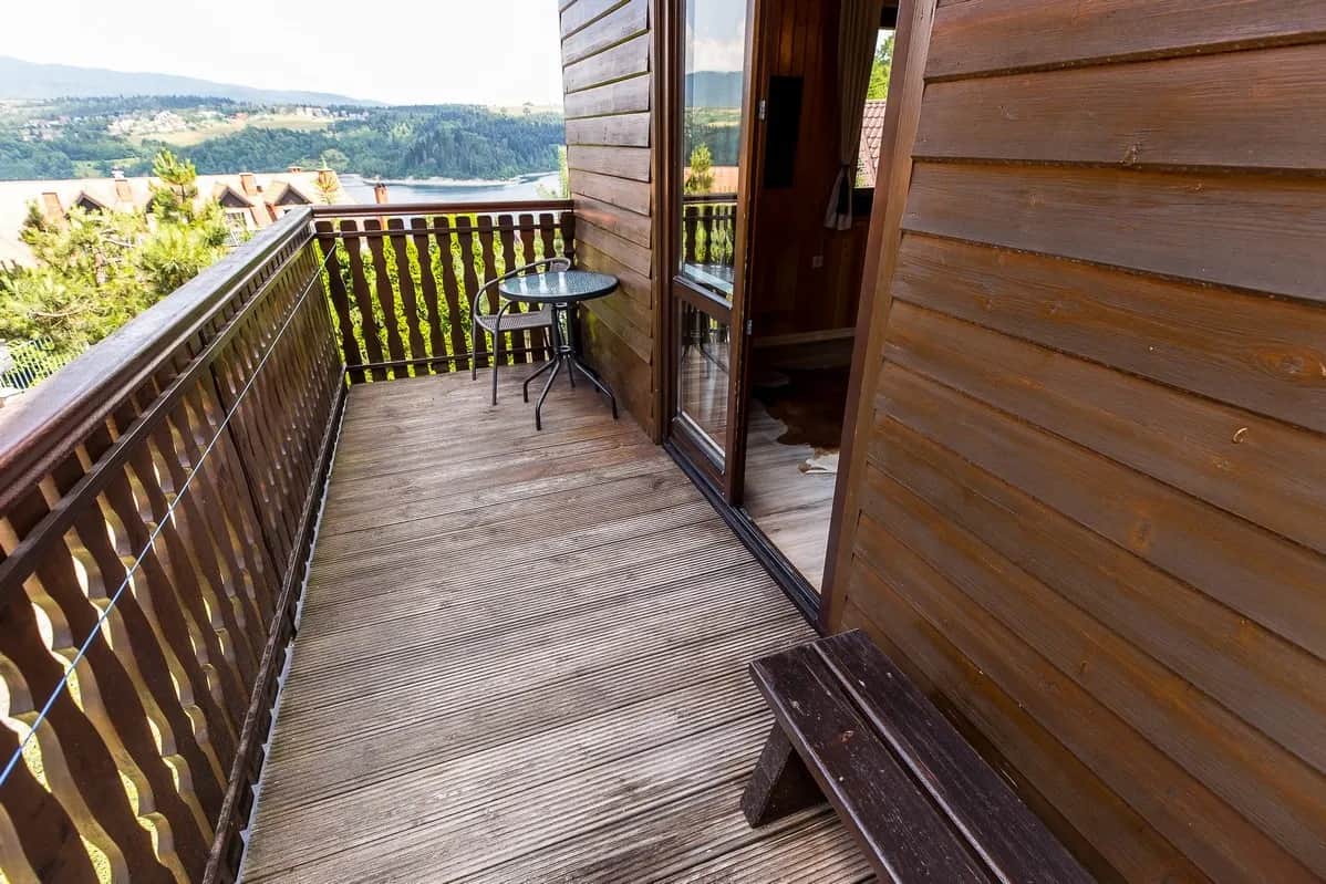Wąski drewniany balkon ze stolikiem i widokiem na jezioro oraz okolicę