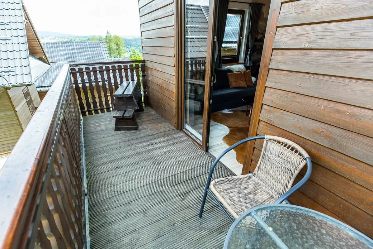 Drewniany balkon z ławką, fotelem i stolikiem oraz widokiem na okolicę