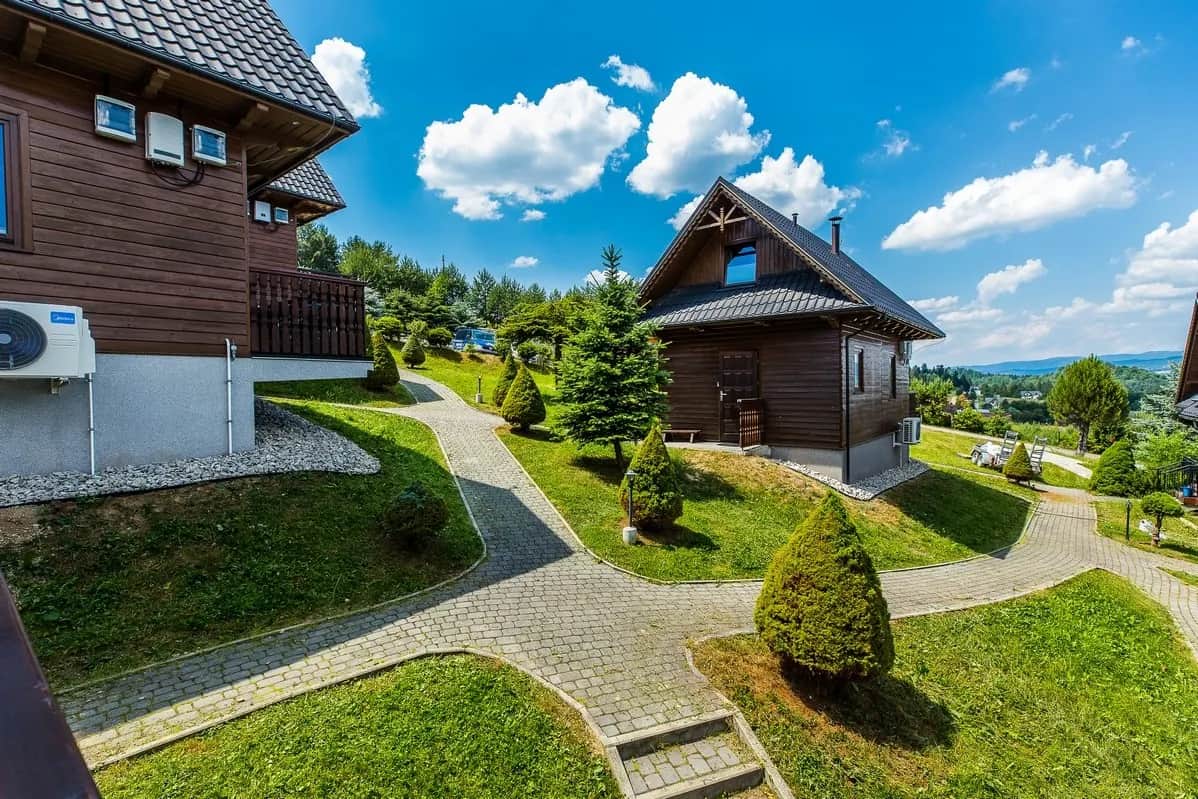 Drewniane domki resortu na zielonym wzgórzu z brukowanymi alejkami i widokiem na góry