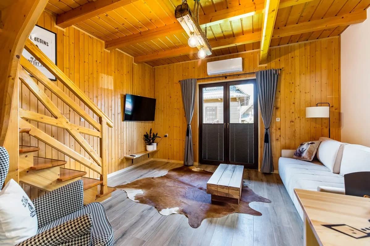 Drewniany salon z telewizorem, schodami na poddasze i przeszklonym wyjściem