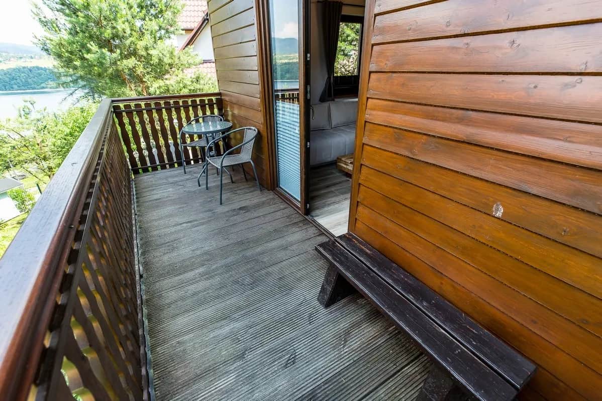 Drewniany balkon ze stolikiem, krzesłami i ławką, w tle jezioro