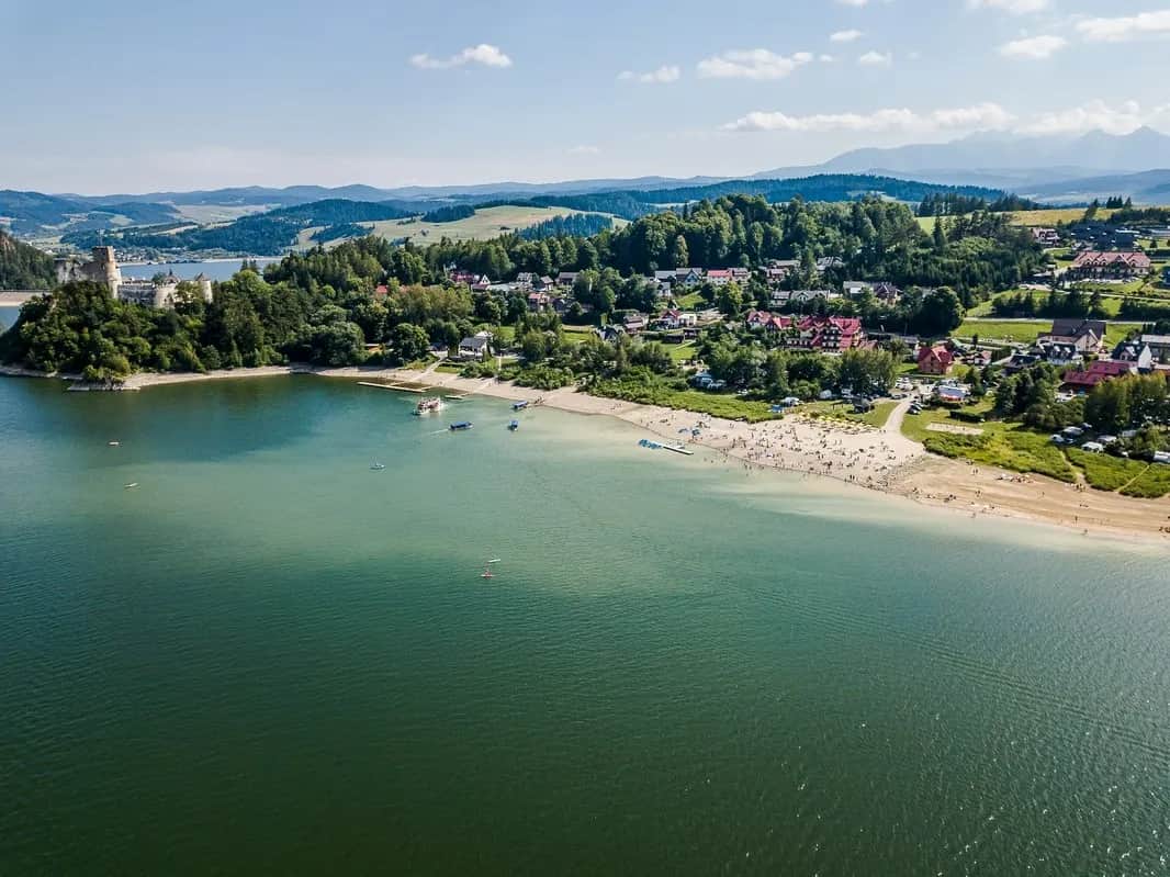 Strand am See mit Burg auf der Landzunge und Bergen im Hintergrund