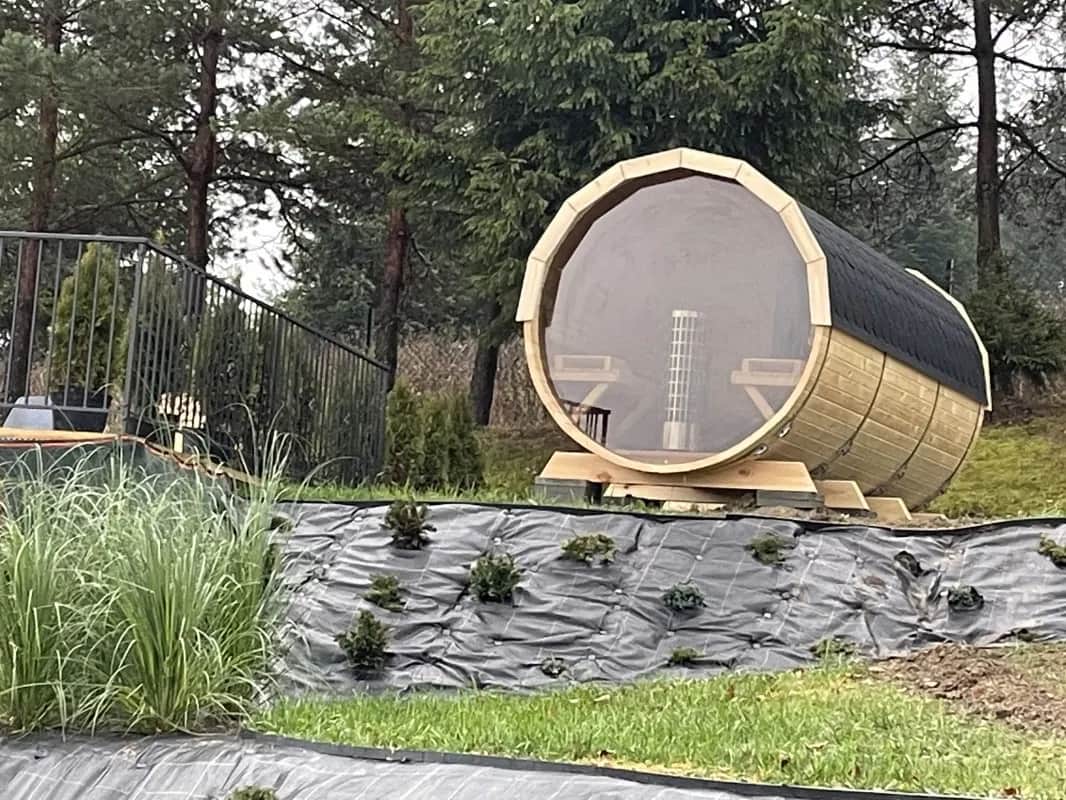 Hölzerne Fasssauna auf einer eingezäunten Terrasse zwischen Kiefern